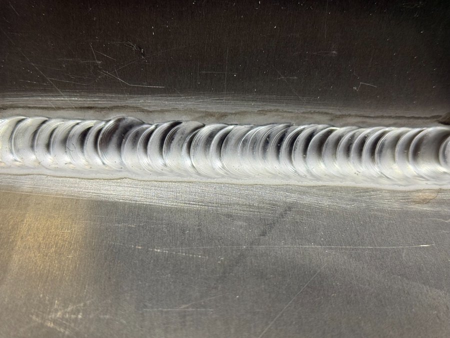 アルミ厚物のTIG溶接ビードを拡大撮影した画像。連続した均一ビードが溶接技術の精度を示す。